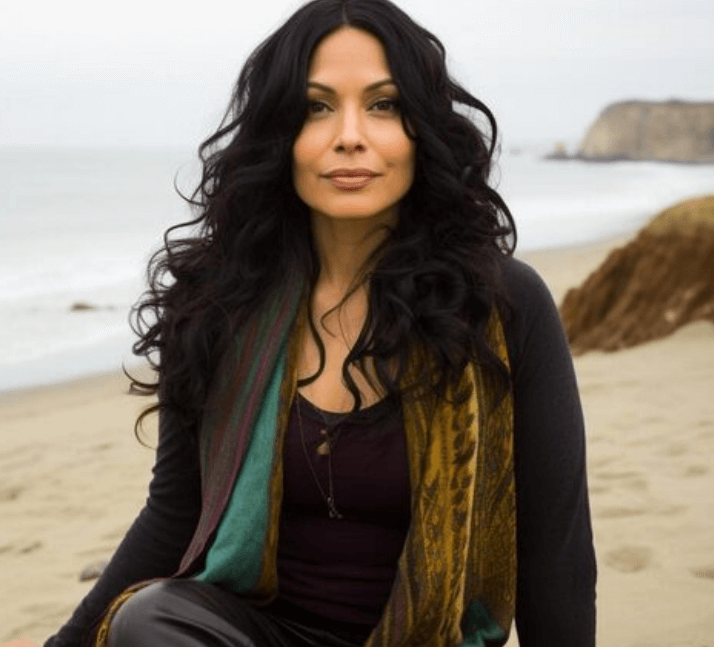 Adult woman with long dark hair sitting on a beach