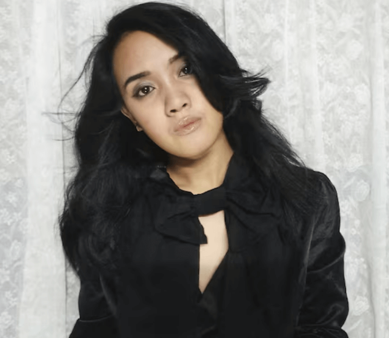 Adult woman in a dark blouse in front of a soft curtain background